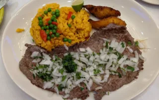 a grilled steak covered in onions and a side of yellow rice