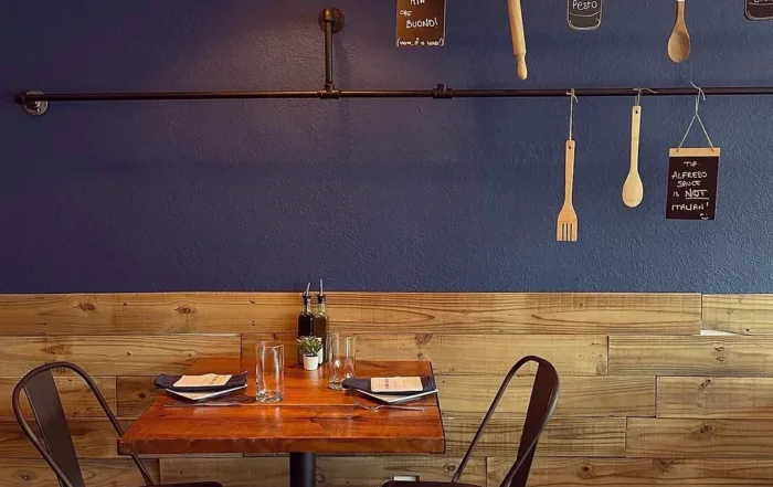 An empty table for 2 against a blue wall with hanging kitchen utensils