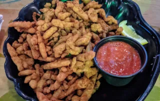 A large bowl of fried clam strips and a small cup of cocktail sauce