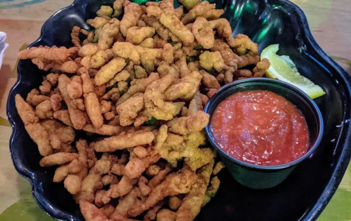 A large bowl of fried clam strips and a small cup of cocktail sauce