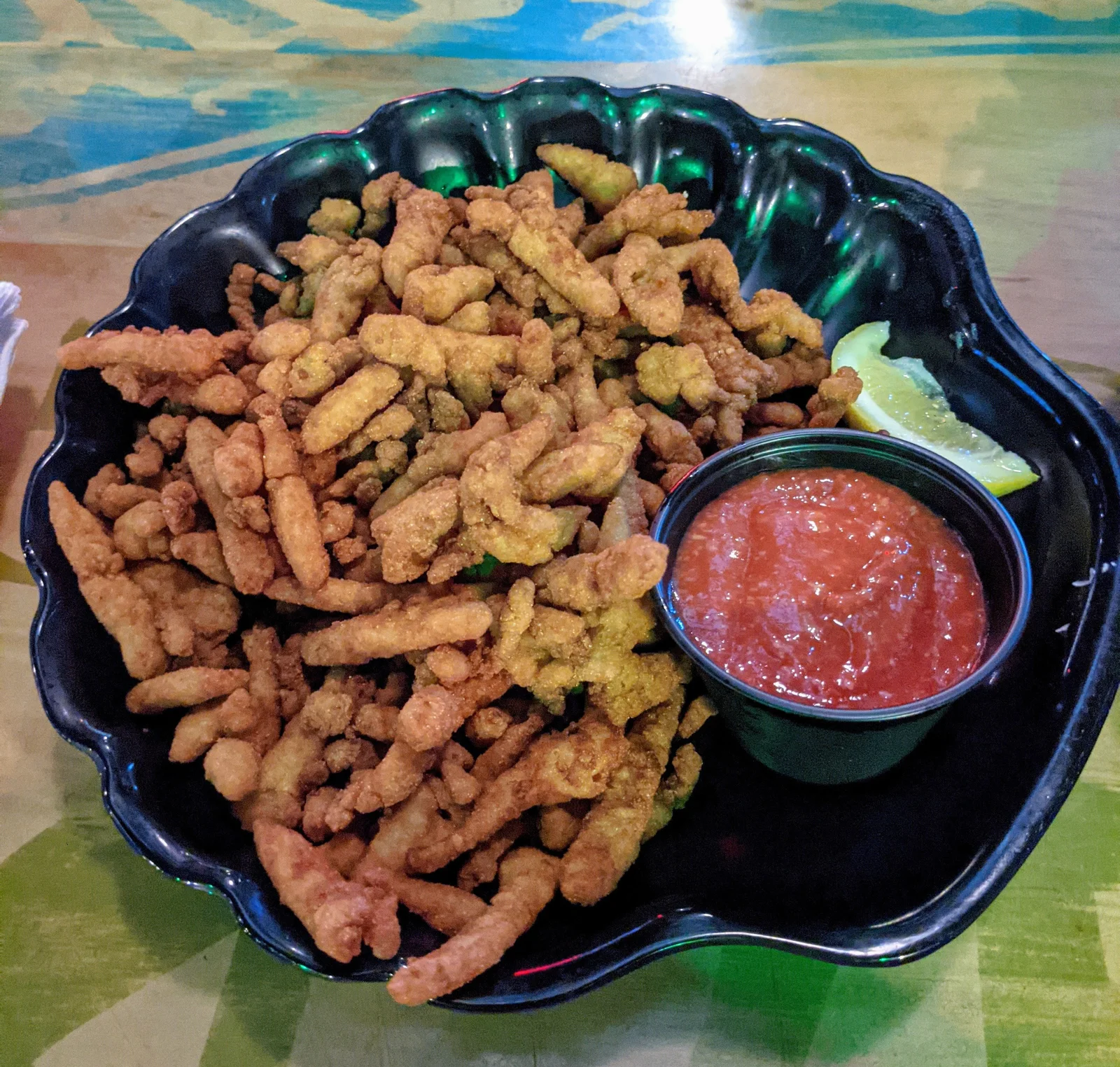 A large bowl of fried clam strips and a small cup of cocktail sauce